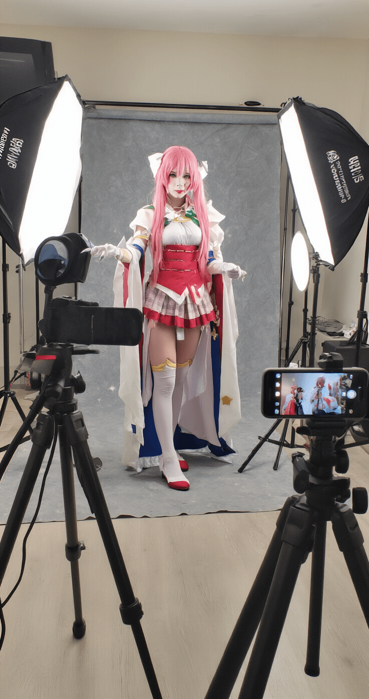 The Ultimate Guide to Anime Cosplay: From Beginner to Pro Professional photography studio featuring a cosplayer in anime character makeup, with soft box lighting, reflectors, and backdrop options visible. A smartphone on a tripod captures the scene from the photographer's perspective.