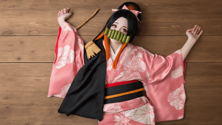 A colorful flat lay of Nezuko cosplay items including a pink silk kimono, black haori coat, bamboo muzzle prop, and a black-to-orange ombré wig, all beautifully arranged on a wooden surface with soft natural lighting.