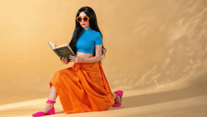 A confident woman in Nico Robin cosplay wears a blue cropped top and orange sarong, holding an archaeology book, with long black hair, pink shoes, and sunglasses, set against a warm golden hour backdrop.