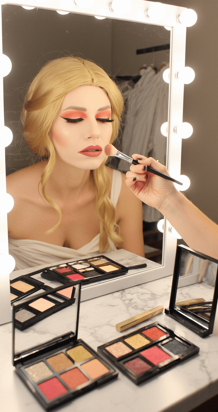 My Hero Academia Cosplay: The Ultimate Guide to Bringing Your Favorite Heroes to Life A woman applies character makeup in a minimalist vanity setup featuring a Hollywood-style bulb mirror, with professional brushes and vibrant eyeshadow palettes on a white marble surface. A half-completed Toga costume is in the background. The close-up profile shot highlights her focused expression and the golden blonde wig pinned back under warm tungsten lighting.